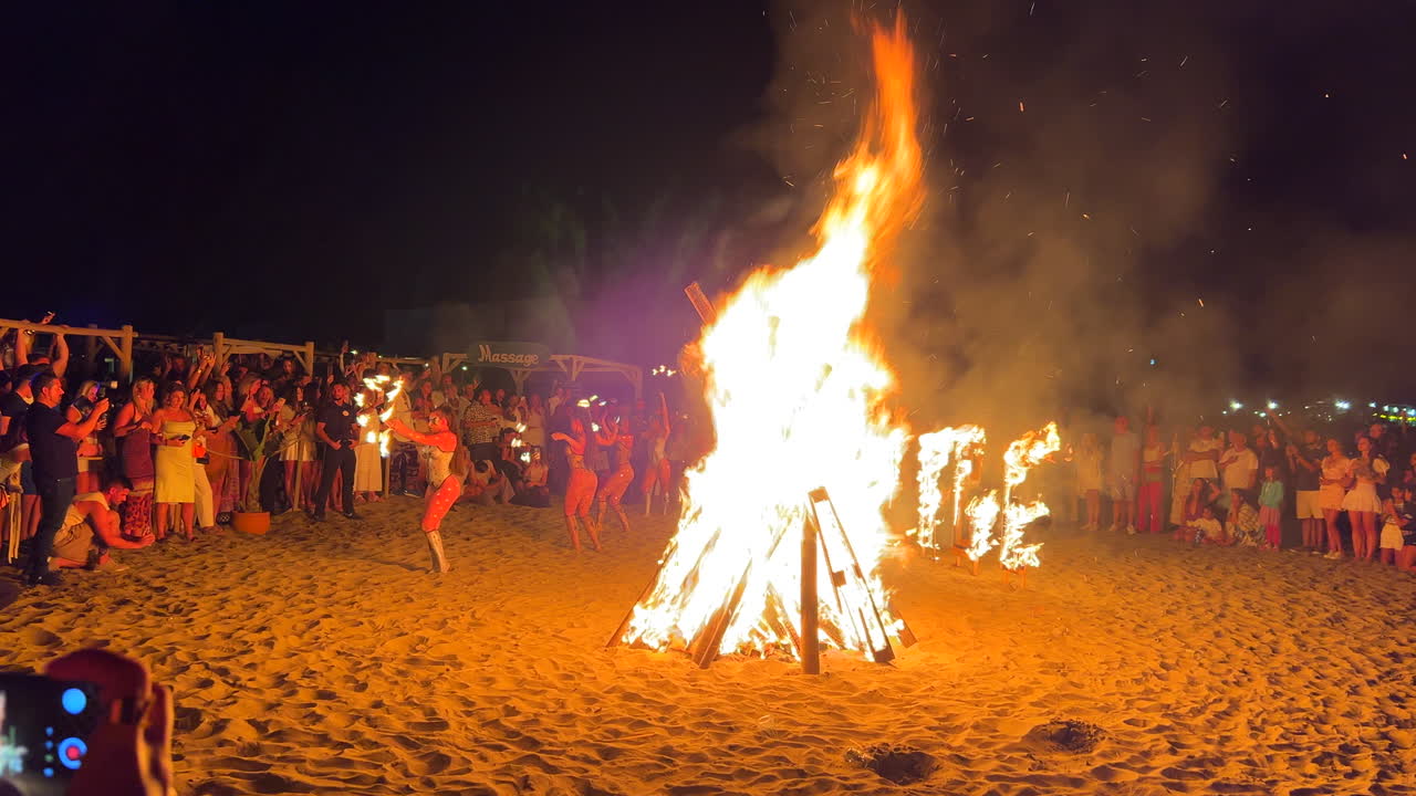 Exotic fire dancers dancing at traditional bonfire summer festival at the beach at the San Juan celebration in Marbella Spain, enjoying a fun party, big burning fire and hot flames at night, 4K shot