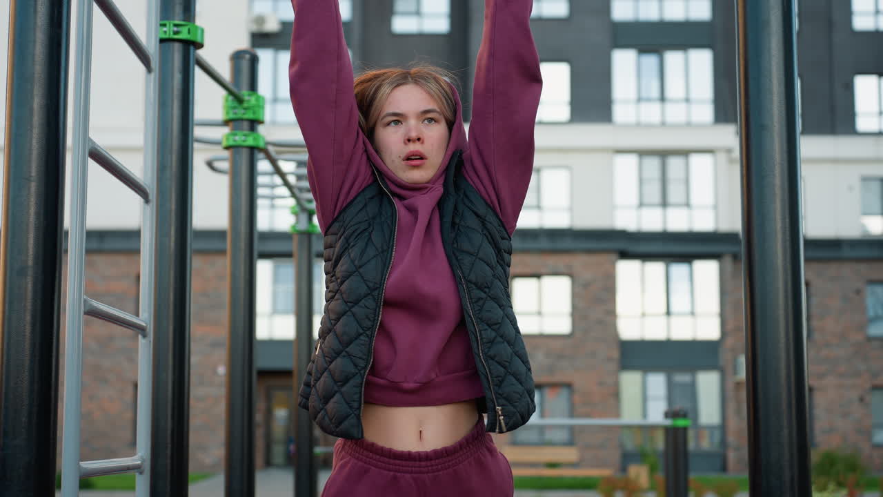 Outdoor urban park workout featuring female fitness coach gripping pull up bars while lifting legs to strengthen core muscles improve balance enhance endurance in bodyweight training session