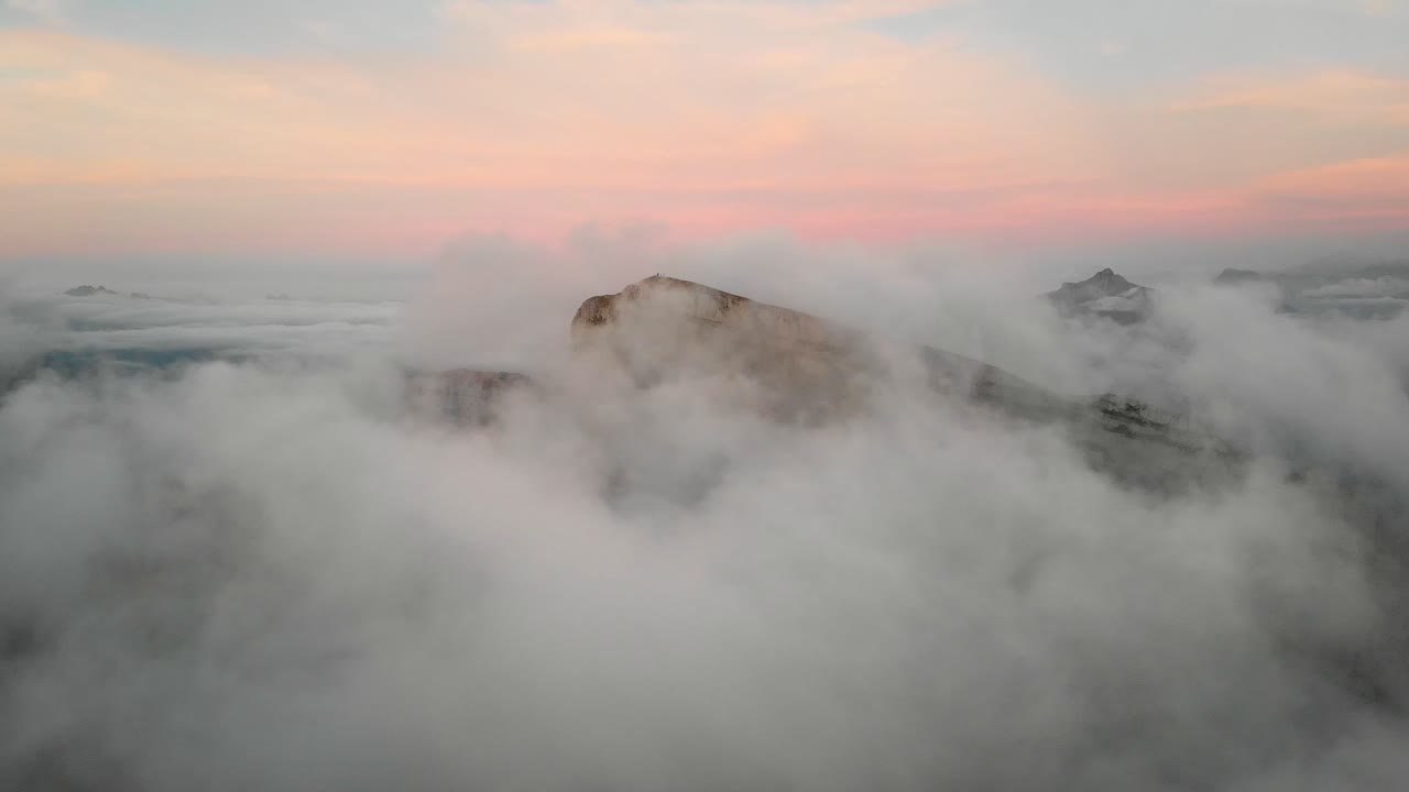 Aerial flyover through clouds in Leysin, Vaud, Switzerland during a colorful autumn sunset with hikers on Tour d'A&iuml; enjoying the panoramic view above clouds with Tour de Mayen in the background