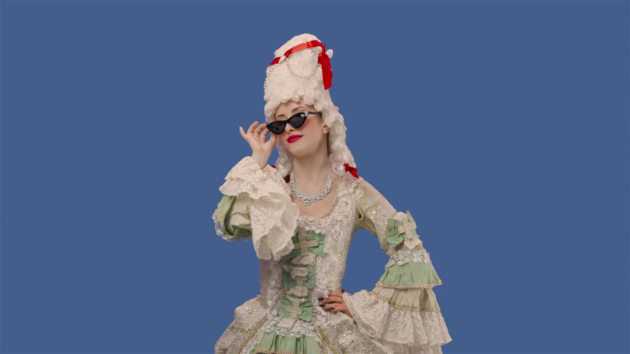 색 빈티지 렌즈 드레스, 위그, 선글라스를 입은 궁정 여자의 초상화, 미소 짓고 유혹하는 젊은 여성이 블루 스크린 배경으로 스튜디오에서 포즈를 취하고 있습니다.