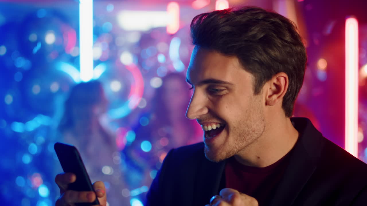 Uomo allegro che usa il cellulare a una festa. Ragazzo felice che legge un messaggio in discoteca.