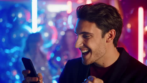 Positive-man-using-mobile-phone-at-party.-Happy-guy-reading-message-in-nightclub