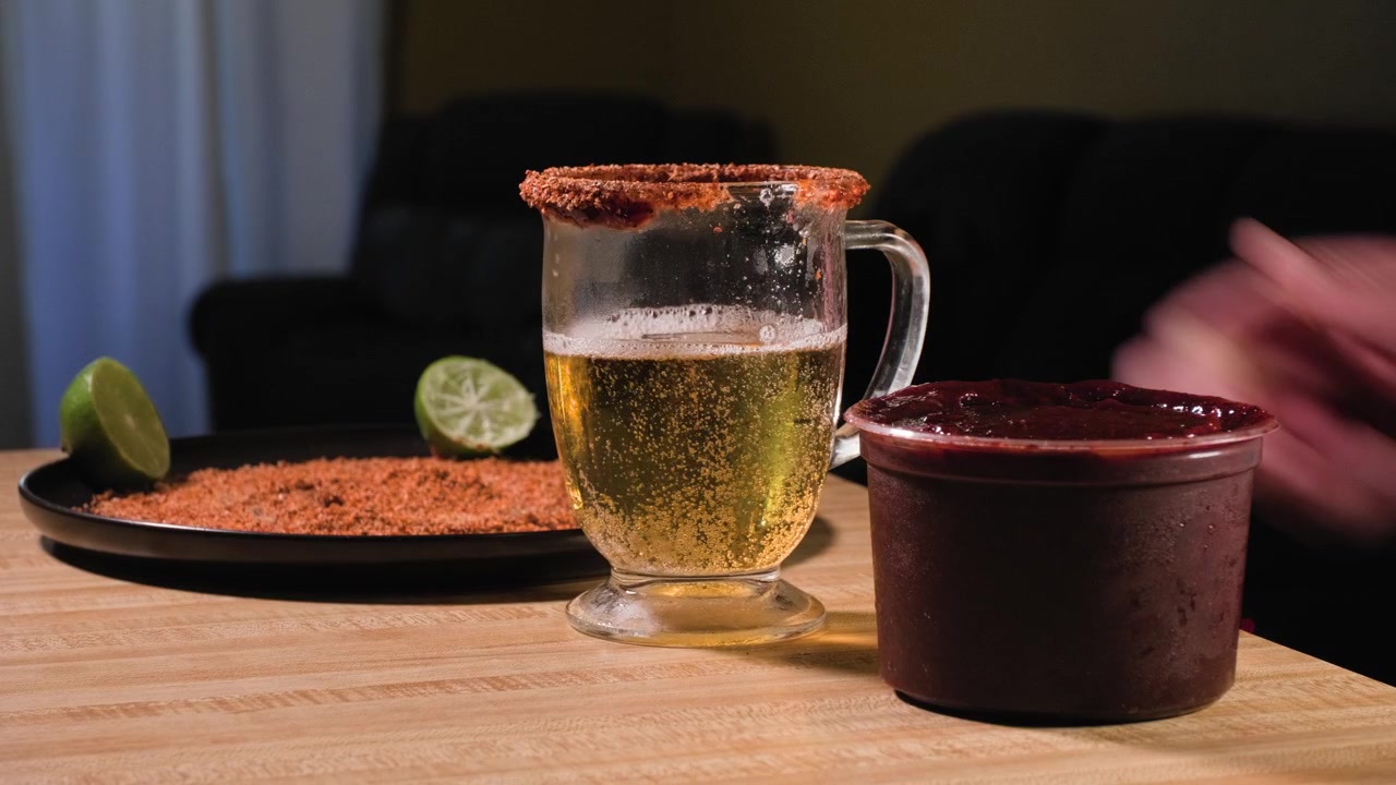 Un hombre coloca un vaso de cerveza escarchado de nuevo sobre una mesa de madera mientras se forman burbujas de carbonatación dentro de la bebida fría.