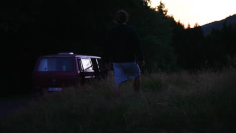 young man walking in a corn field near a rer old retro bus, van towardsthe sudown