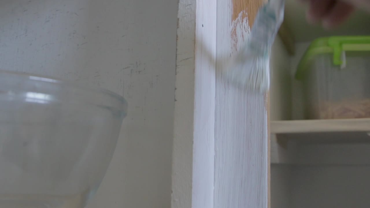 locked off man painting a wooden structure white with paintbrush