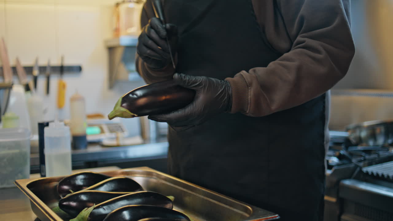 Chef sconosciuto che prepara melanzane in una cucina professionale di un ristorante, primo piano