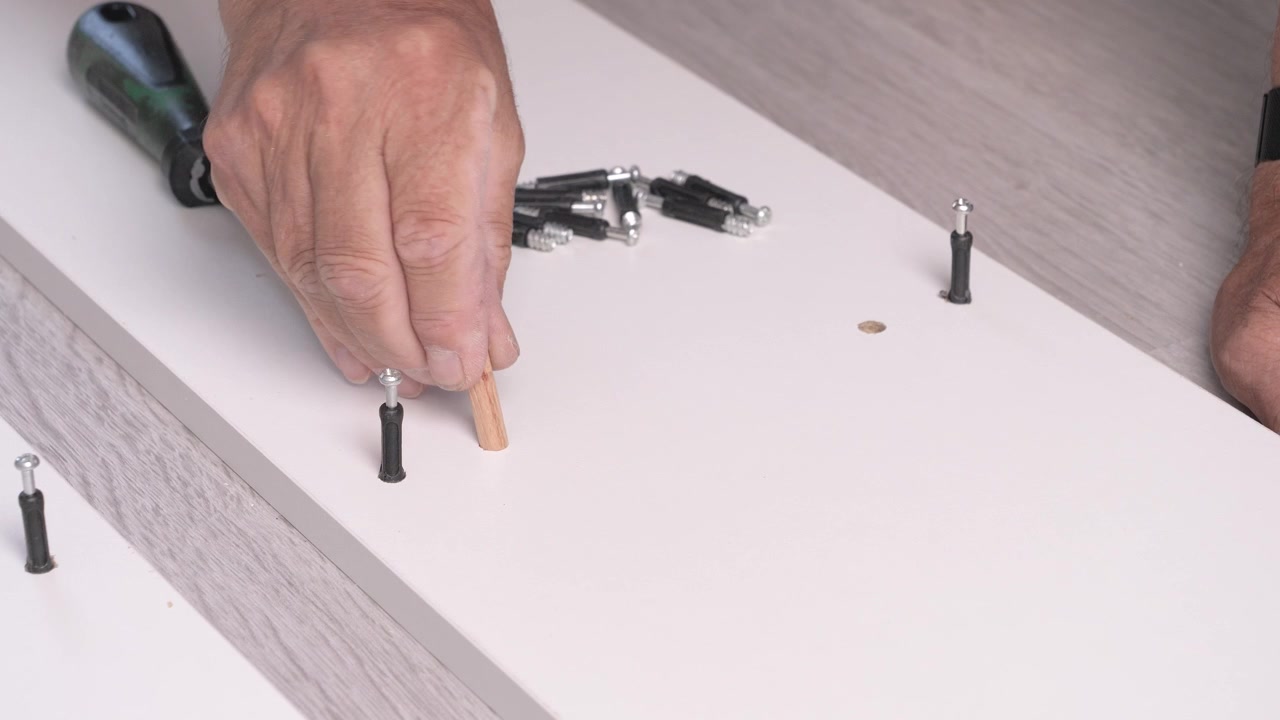 Installing of cabinet furniture parts at home, close-up of male hands screws a screw.
