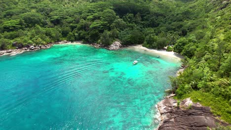 Drone-shot-heading-to-anse-major-beach,-ocean,-rich-forest,-granite-rock-and-turquoise-water,-docking-boat,-Mahe-Seychelles-30-fps