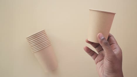 hand holding a brown paper cup, with stacked cups in the background