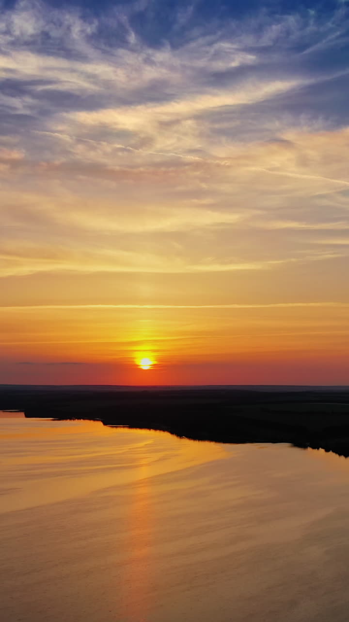 Calm water of the evening lake. Aerial view on the river among natural forests and fields at sunset. Camera moves back. Vertical video