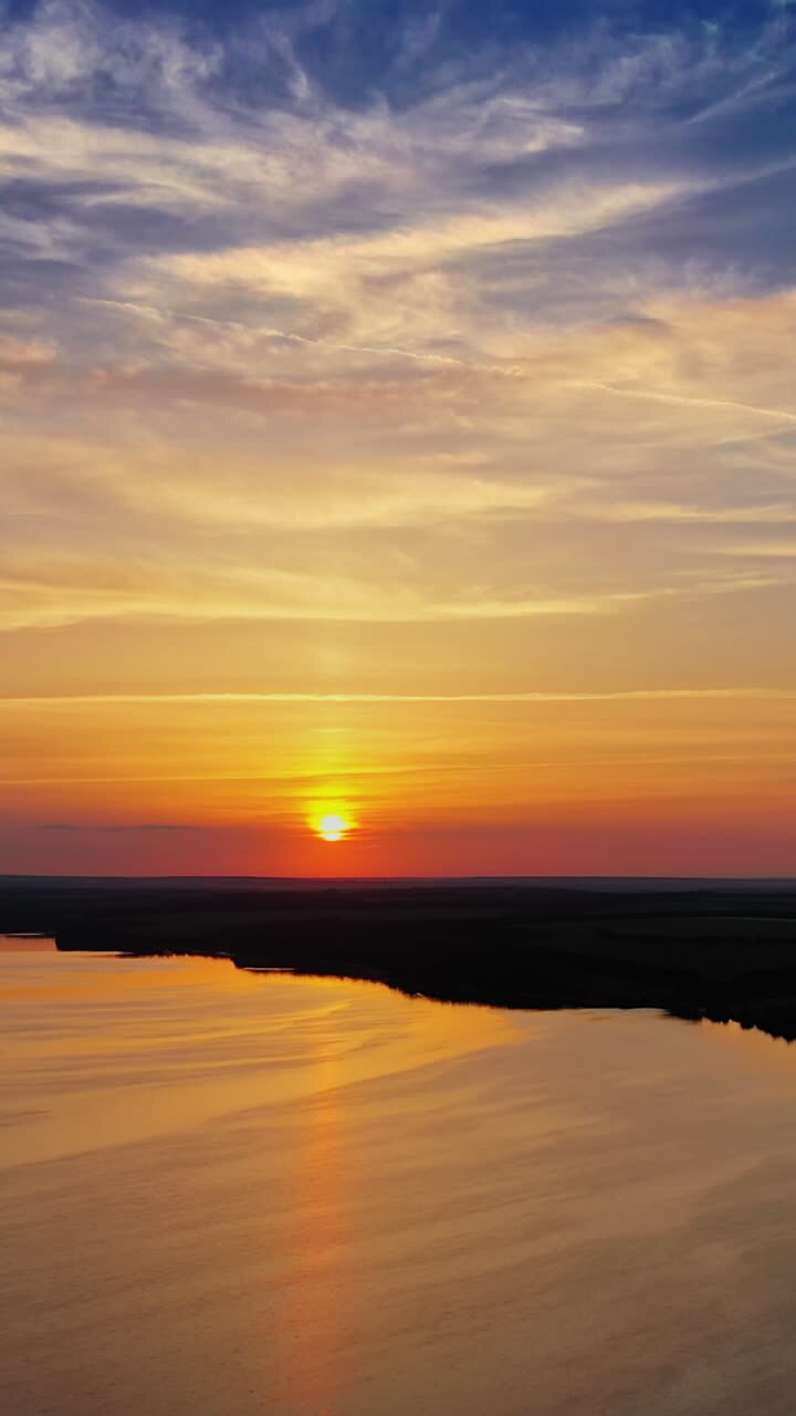 Calm water of the evening lake. Aerial view on the river among natural forests and fields at sunset. Camera moves back. Vertical video