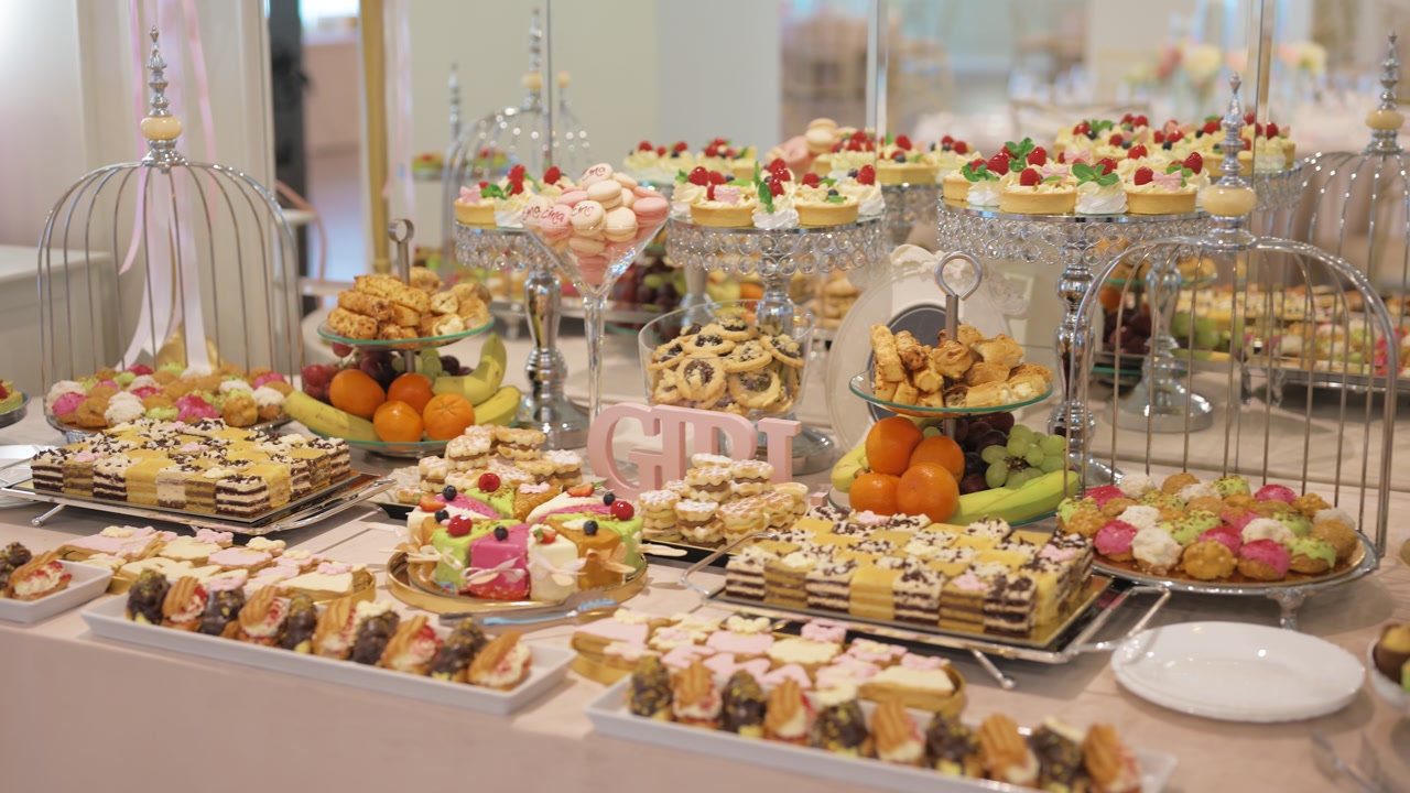 Dessert table filled with a wide variety of colorful sweets, pastries, fruits, and decorative elements, captured in a bright indoor event setting