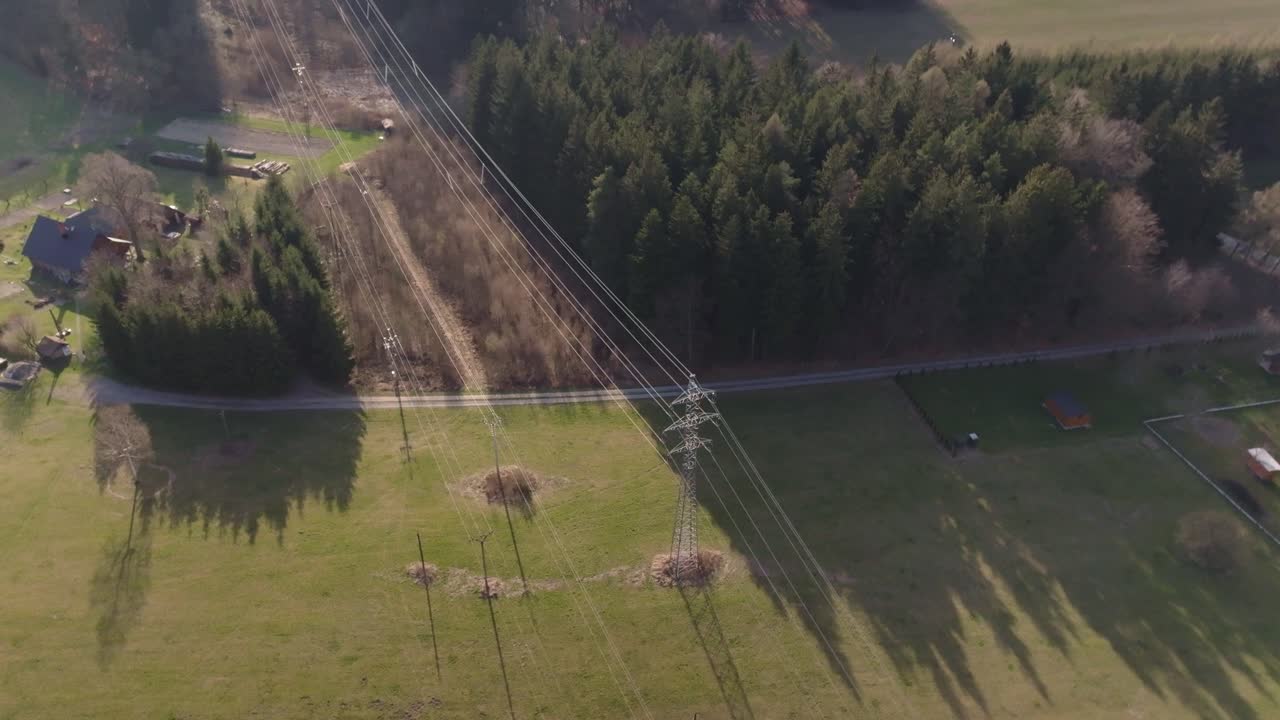 High voltage switchboards and wires. Large towers carrying cables through hills and nature. Aerial drone shot