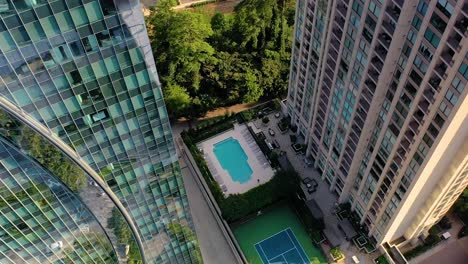 Slowly-tilting-down-drone-shot-of-a-swimming-pool-and-tennis-court-between-two-skyscrapers-in-Buckhead,-Atlanta,-Georgia