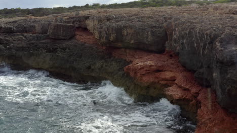 AERIAL:-Close-Up-of-Waves-crashing-into-Rocks,-Cliff,-Coast-on-Sunny-Day-on-Mallorca-Island-Sunny-Weather,-Sunshine