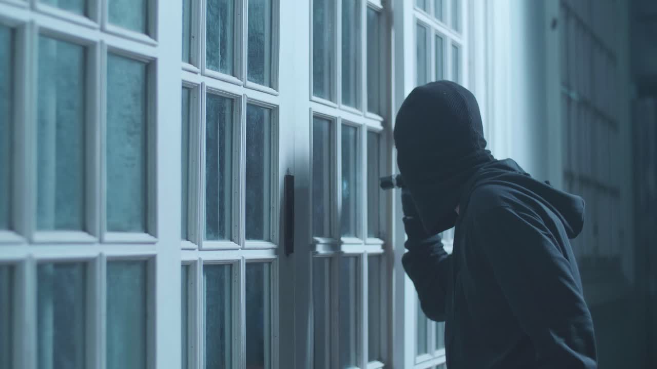 ladrón hombre con linterna y palanca mirando dentro de la casa mientras está de pie afuera en la noche oscura