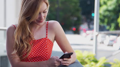 joven mujer de negocios de pie fuera del edificio de oficinas de la ciudad usando teléfono móvil