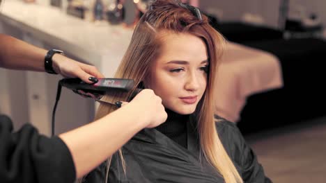 hermosa chica en un salón de belleza sostiene la alineación del rizador de cabello