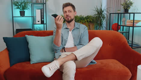 excited young man making phone conversation with friends sitting call on couch at home in room