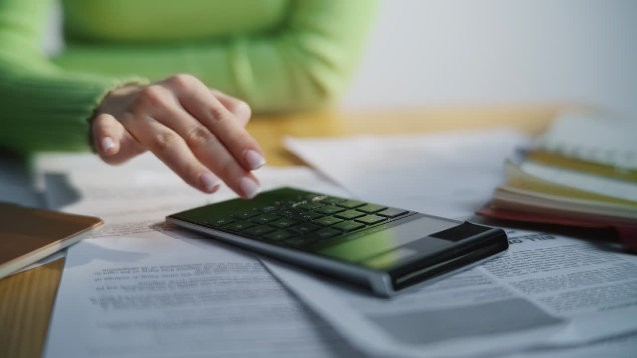 Accountant fingers pushing calculator buttons at table full of documents closeup