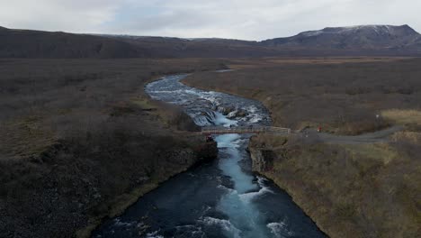 Menschen-Auf-Der-Holzbrücke-über-Den-Bruararfoss-Wasserfall-Und-Die-Umliegende-Landschaft,-Island