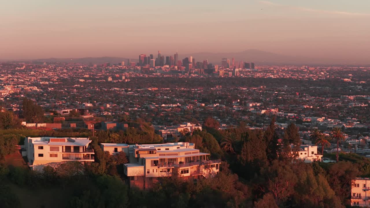 Ripresa aerea con carrello e teleobiettivo di case di celebrità a Hollywood Hills con vista sul centro di Los Angeles al tramonto nella California del Sud. 4K.