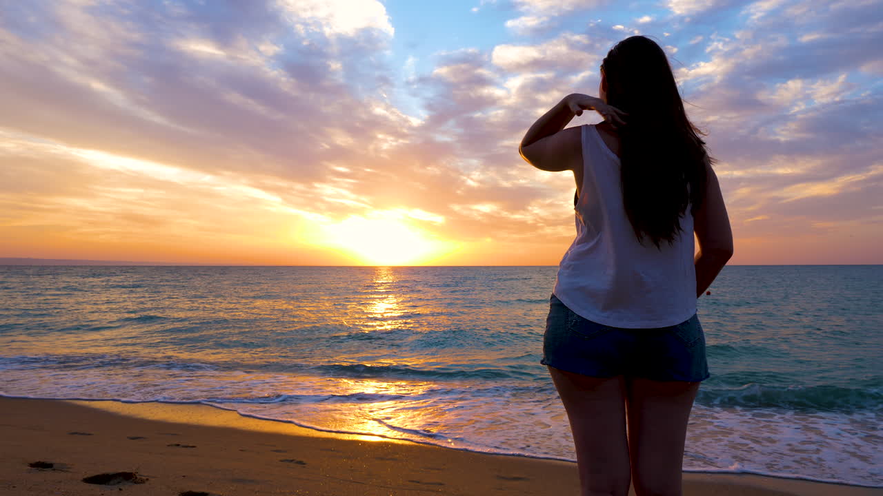 Young woman admiring a gorgeous, vibrant sunrise on the beach