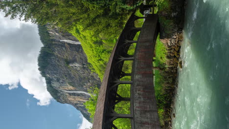 vertical 4k timelapse, idyllic village in swiss alps, wooden footbridge, river, waterfalls and green landscape on spring season