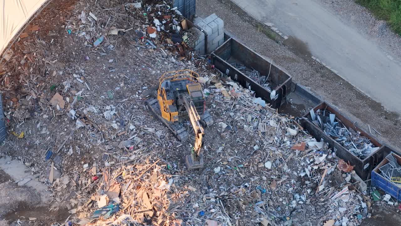 Hochwinkel-Drohnenaufnahme eines Baggers, der Schrott und Müll auf einem Schrottplatz bewegt.