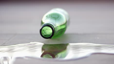 a green glass bottle spills water on the floor