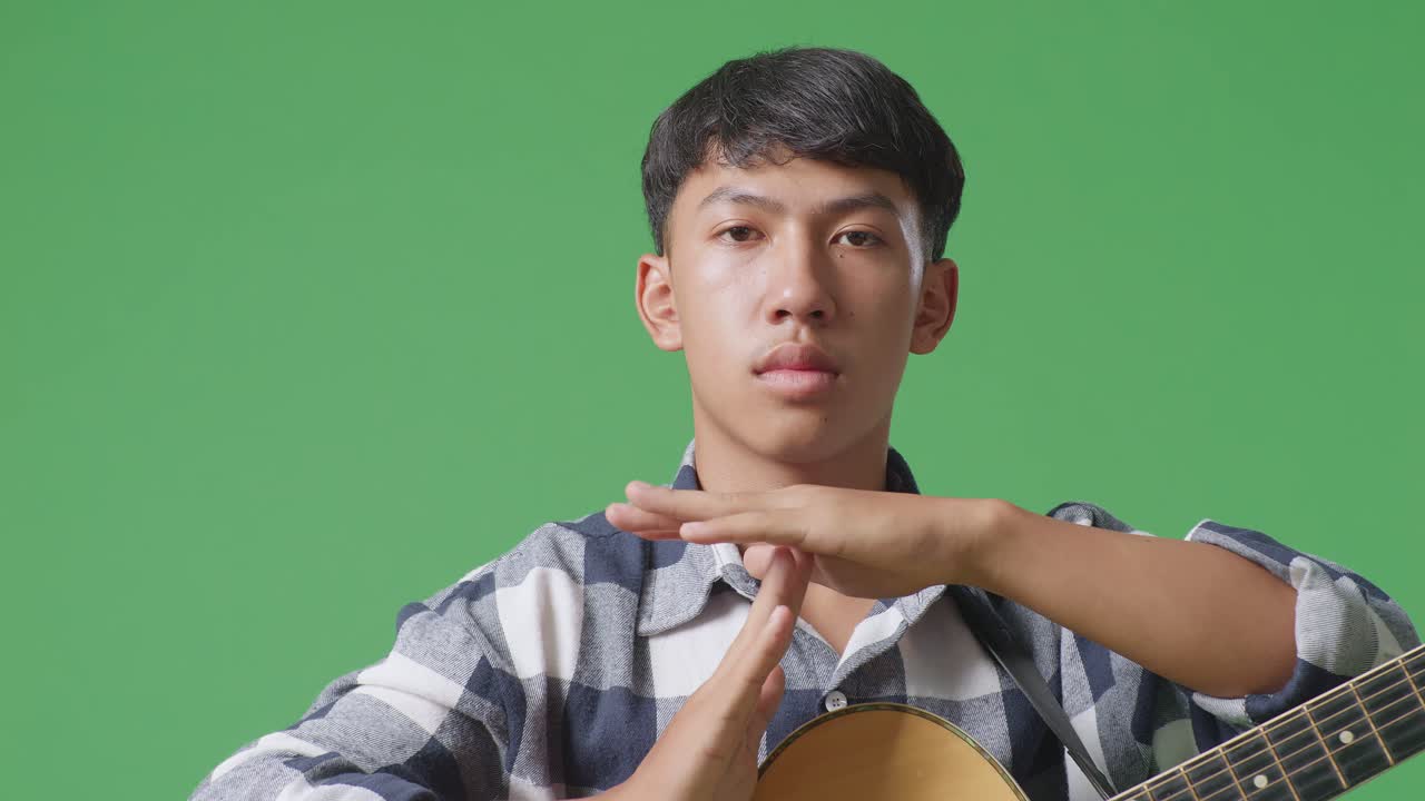 기타를 들고 있는 아시아인 십대의 클로즈업. 녹색 스크린 배경에 손을 는 제스처.