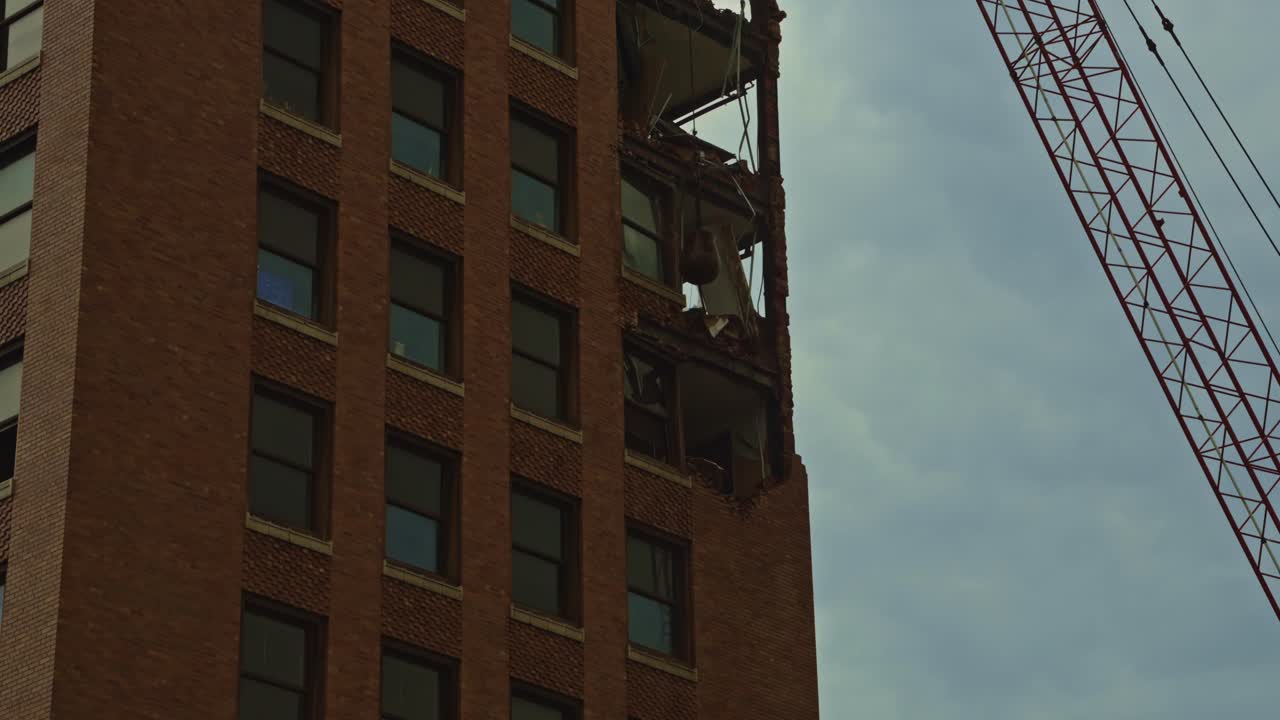Side view of a wrecking ball smashing through the top floors of a high-rise brick building during urban demolition. Dramatic exterior perspective.