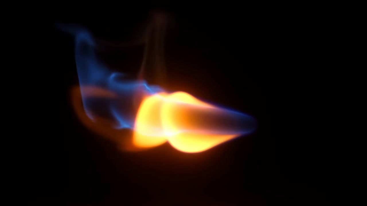 Close-up of isolated orange and blue flame shifting against black background, bright core leaning sideways while cool wisps curl, trail, and glow with vivid contrast and dramatic atmospheric energy