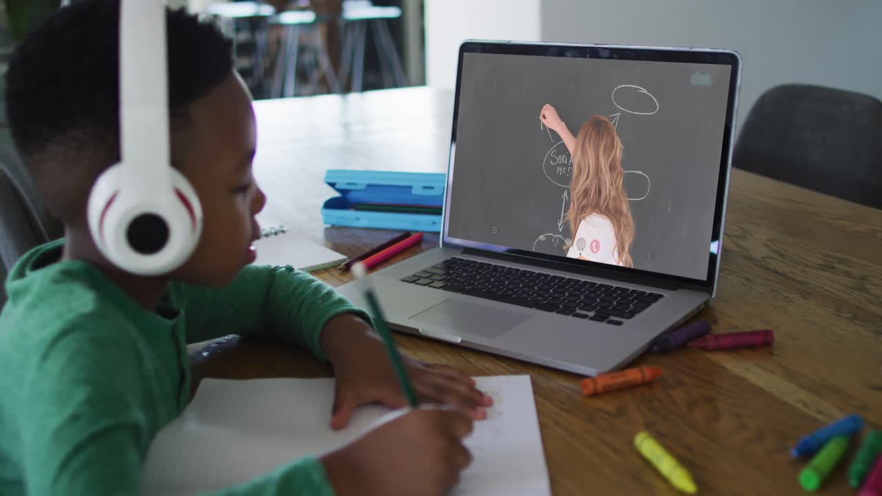 African american boy wearing headphones having a video call on laptop while doing homework at home