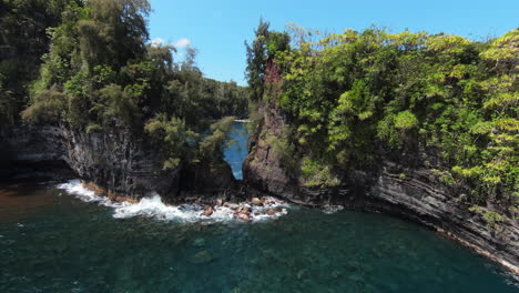 FPV-drone-flies-over-ocean-through-small-gap-in-cliff-on-coast-of-Hawaii