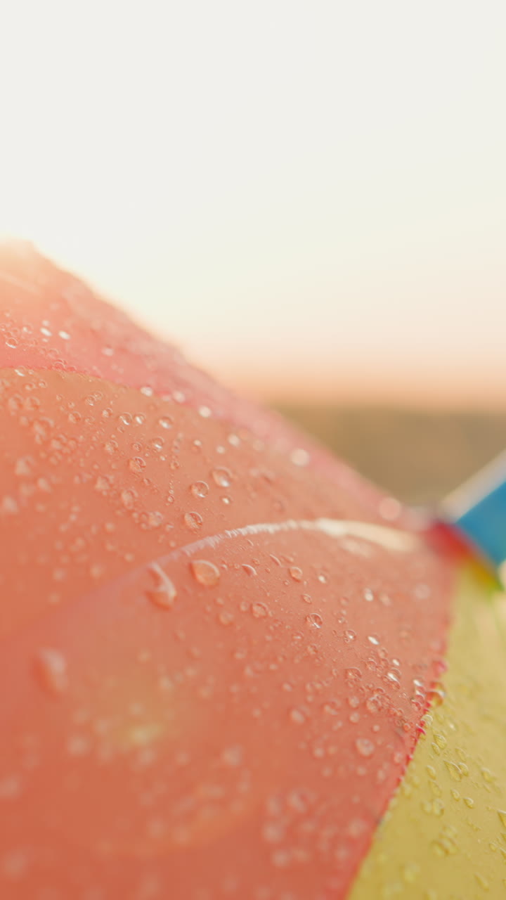 Raindrops fall on bright umbrella surface. Colorful parasol adds cheerful touch to scene with vibrant hues contrasting beautifully with soft gray of spring sky