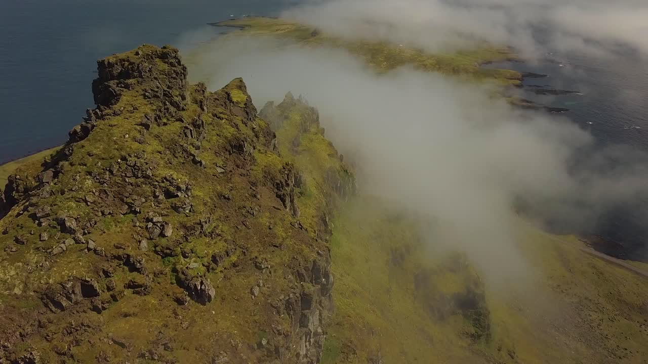 muñeca aérea en verdes colinas empinadas cubiertas de nubes junto al mar, en la pequeña ciudad de djúpivogur cerca de los fiordos de islandia durante el día