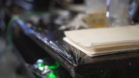 área de la tienda de artistas del tatuaje con fuente de alimentación de luz verde y área de trabajo de envoltura de plástico esterilizada desinfectada con guantes desechables de goma y agujas en el fondo