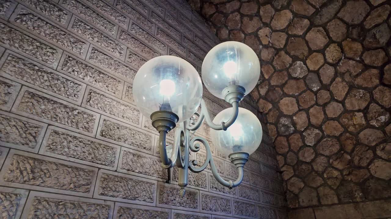 Close-up of lamppost with three illuminated globes on stone wall under famous Pont Alexandre