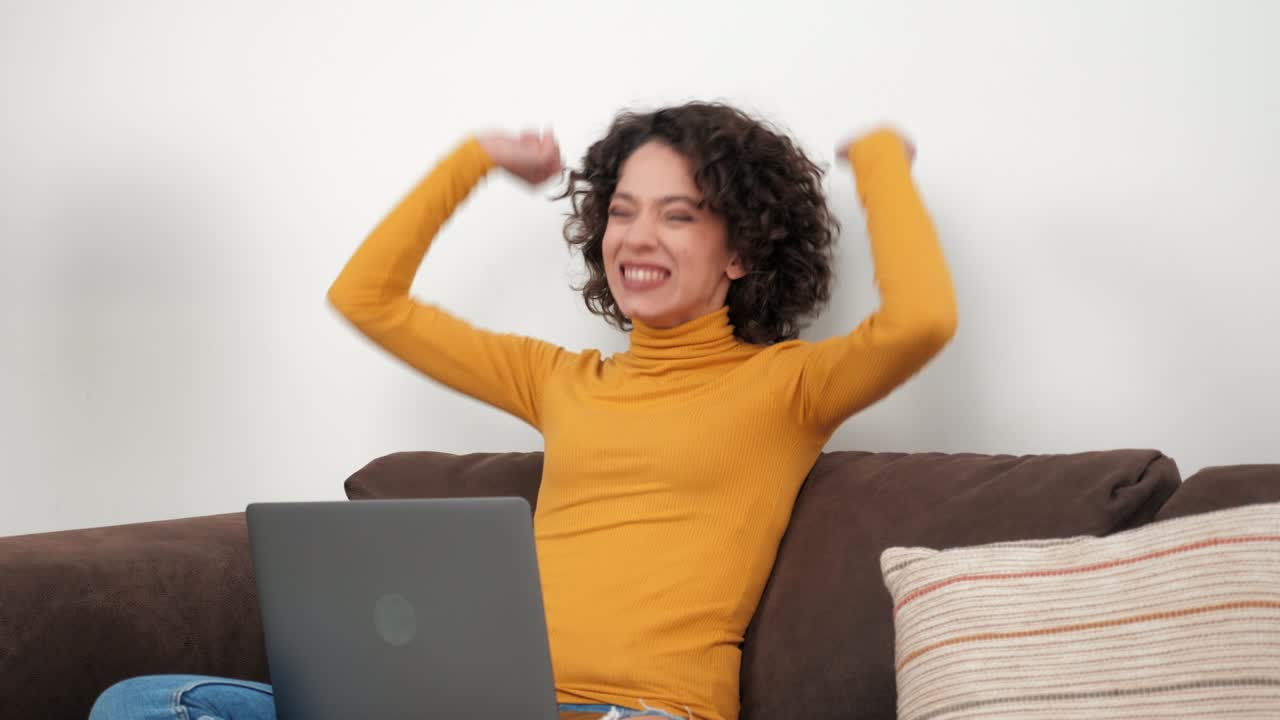Entusiasta studentessa riccia vincitrice che celebra l'ammissione all'università, con laptop