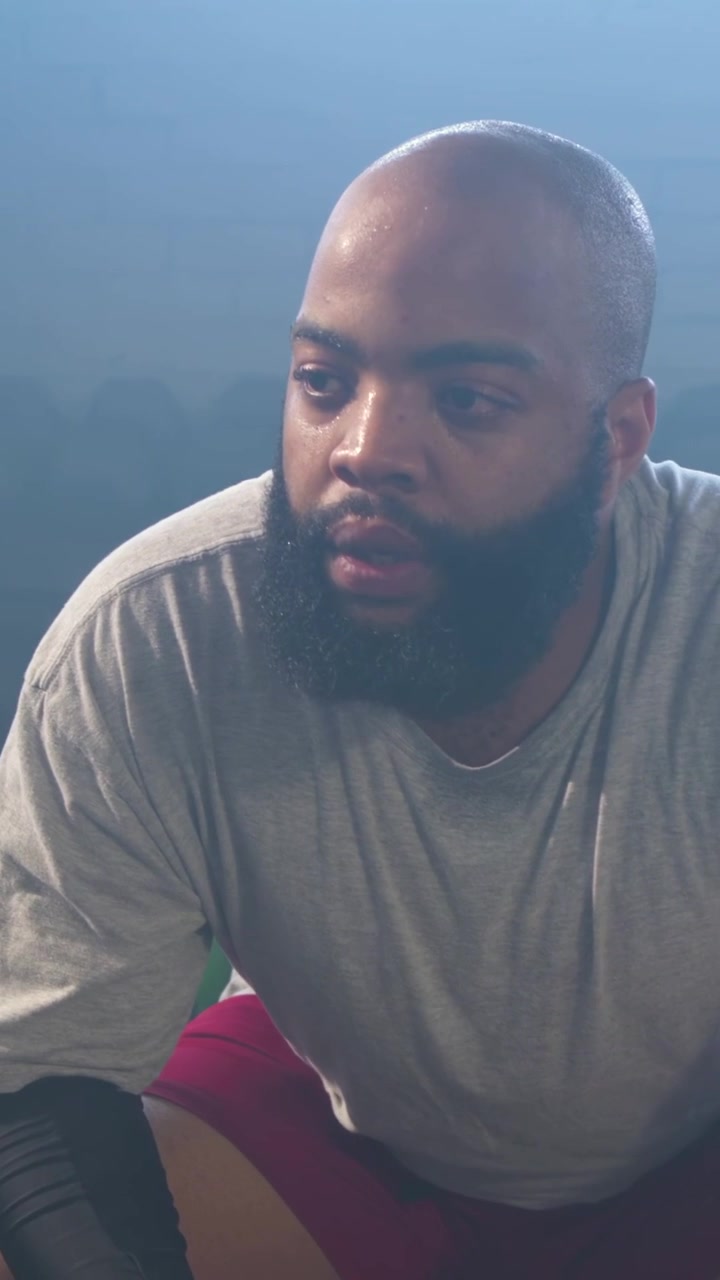 Vertical video: Breathing heavily after set, man on gym bench lifting head to camera, shorts, watch