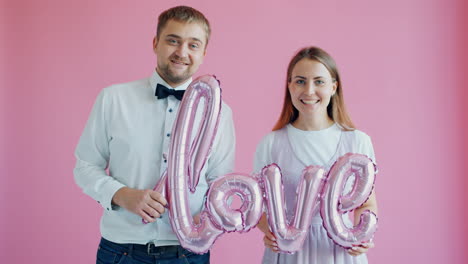 couple holding pink balloons with the word 'love'