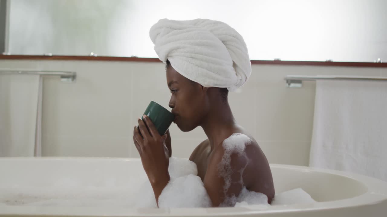Profile of african american attractive woman relaxing in foam bath and drinking coffee in bathroom