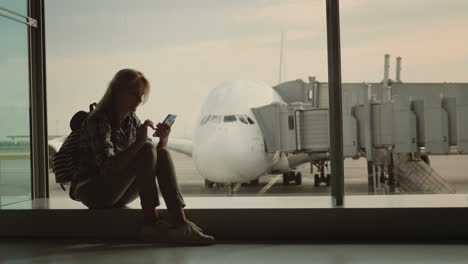 una turista activa con una mochila se sienta en la ventana en el fondo del avión y juega o
