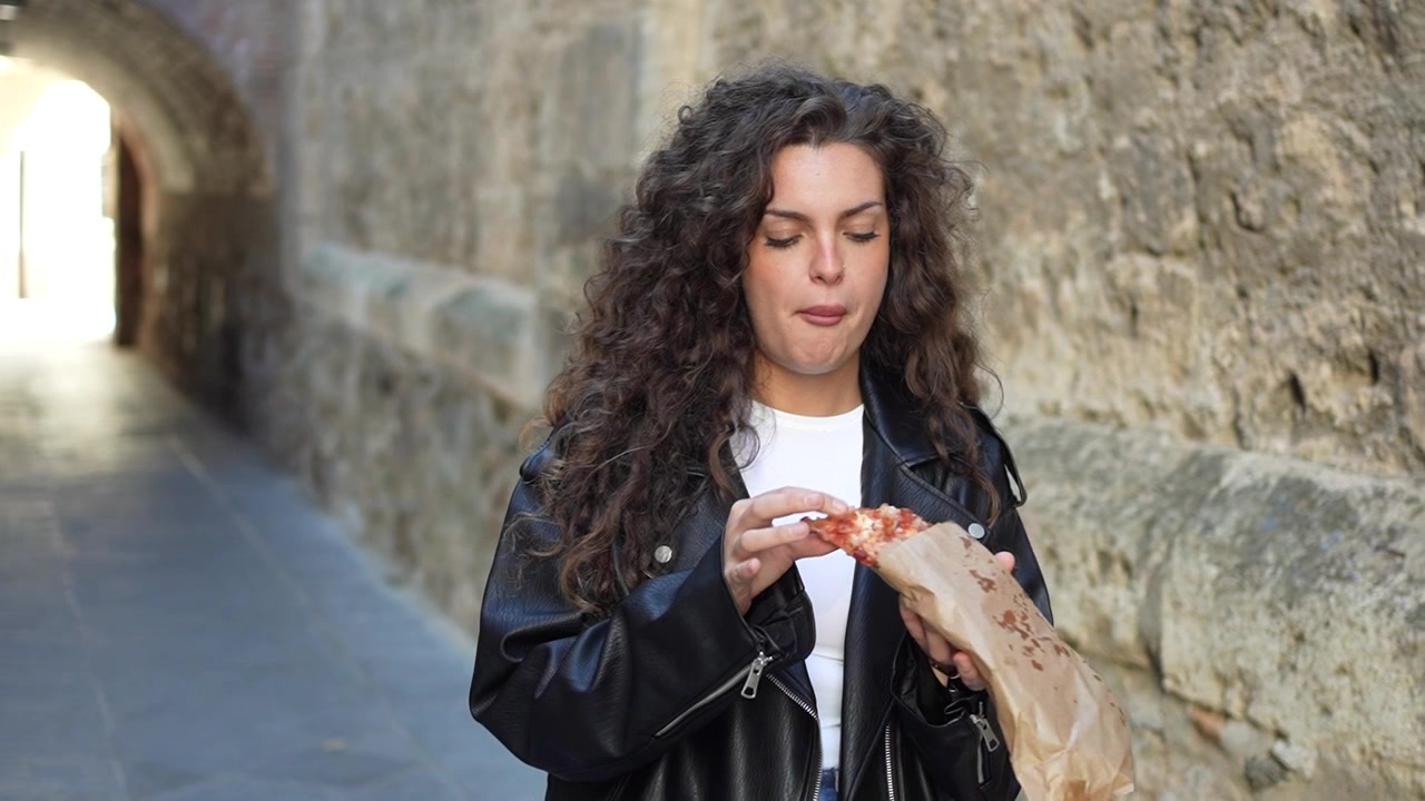 Uma jovem desfrutando alegremente de um lanche numa rua histórica charmosa e pitoresca.