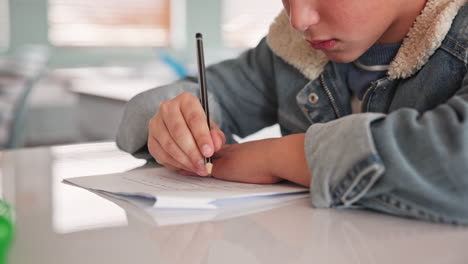 a child writing with a pencil on paper at a desk in a classroom
