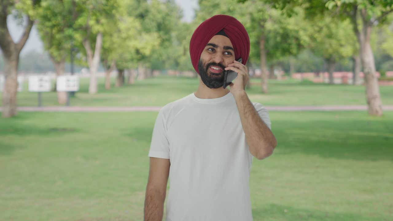 Uomo indiano Sikh felice che parla al telefono al parco.