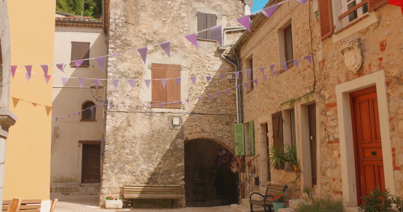 Stretto vicolo in pietra con festoni colorati appesi tra edifici medievali.
