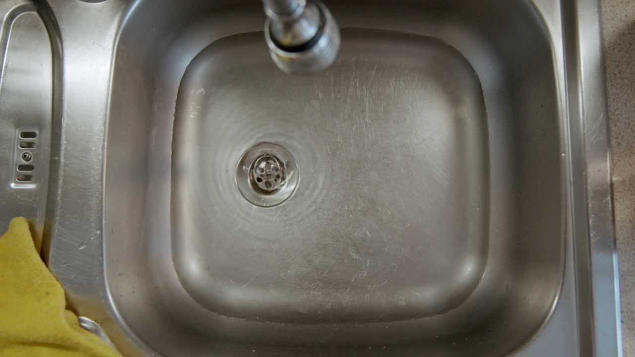 Metal Kitchen Sink Washbasin full of Water Draining through Hole with Swirling Motion in slowmo