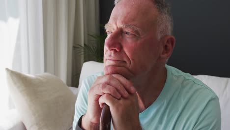 Close-up-of-caucasian-senior-man-holding-walking-stick-while-sitting-on-the-couch-at-home